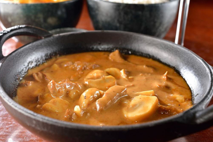 Panela de barro com estrogonofe e potes de arroz atrás.