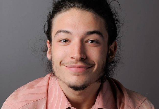 Ezra Miller sorrindo, com uma camisa rosa