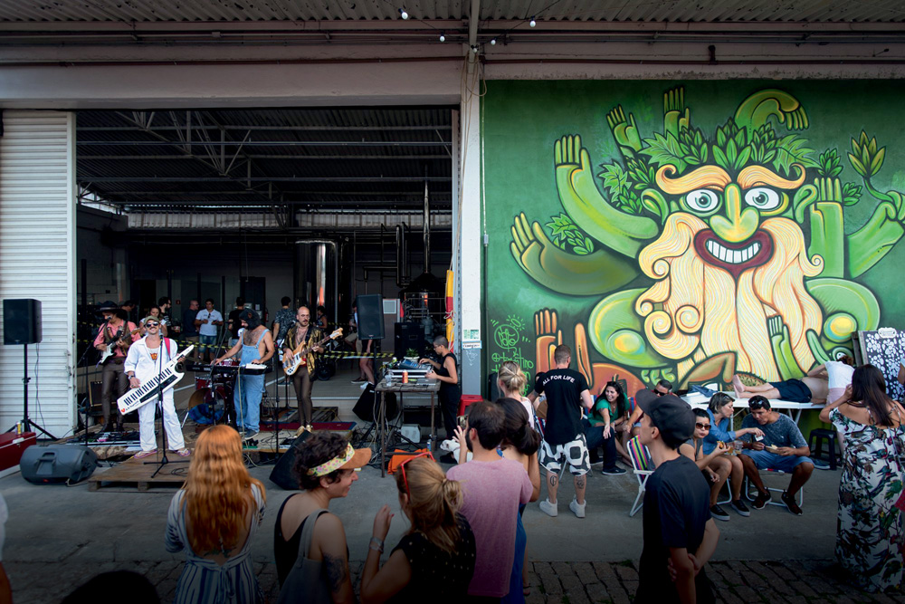 Ambiente da Cervejaria Tarantino repleto de público, que assiste apresentação de banda, ao fundo na foto