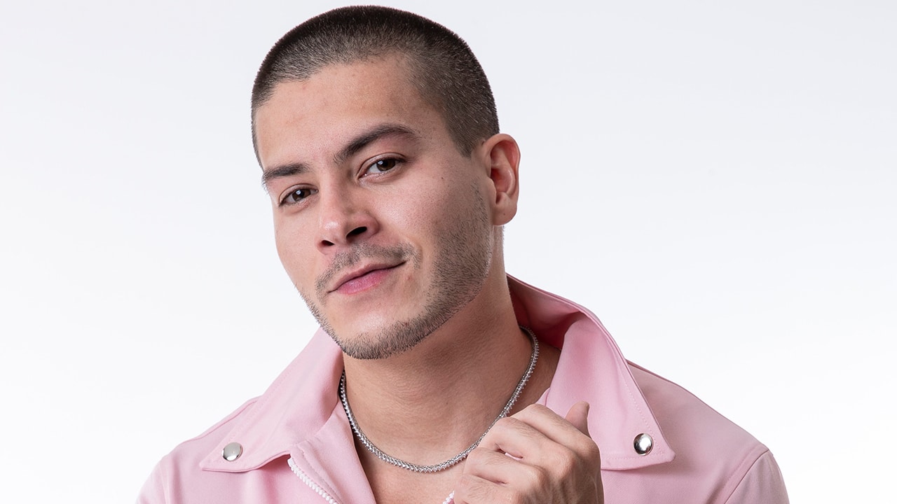 Arthur Aguiar posa com os braços erguidos e mãos apoiadas atrás da cabeça, com expressão de análise. Veste regata preta.