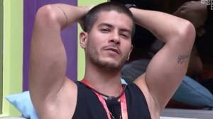 Arthur Aguiar (Reprodução) Arthur Aguiar posa com os braços erguidos e mãos apoiadas atrás da cabeça, com expressão de análise. Veste regata preta.