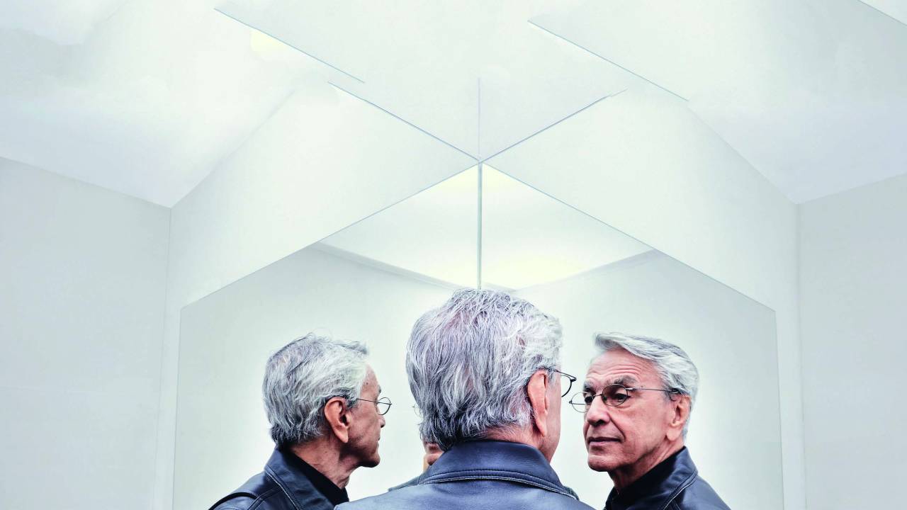 Imagem mostra homem grisalho de costas, refletido por dois espelhos.