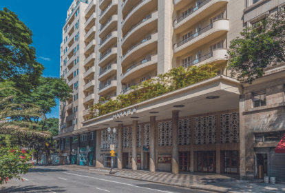 Imagem mostra fachada de hotel branca com pilares e varanda com jardim no primeiro andar