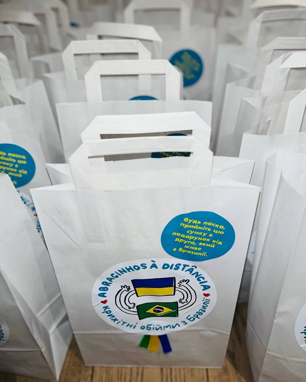 Fileira de sacolas brancas com logotipo que exibe as bandeiras da Ucrânia e do Brasil.