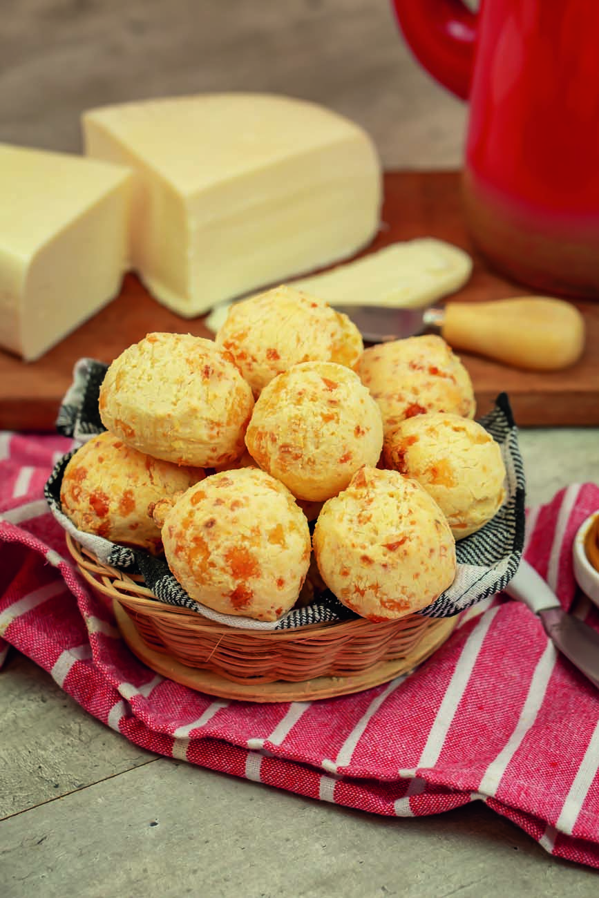 Taça de vidro com sorvete sobre base redonda de madeira, com pedaço de goiabada, pedaço de queijo e pequena faca ao lado, sobre mesa de madeira branca