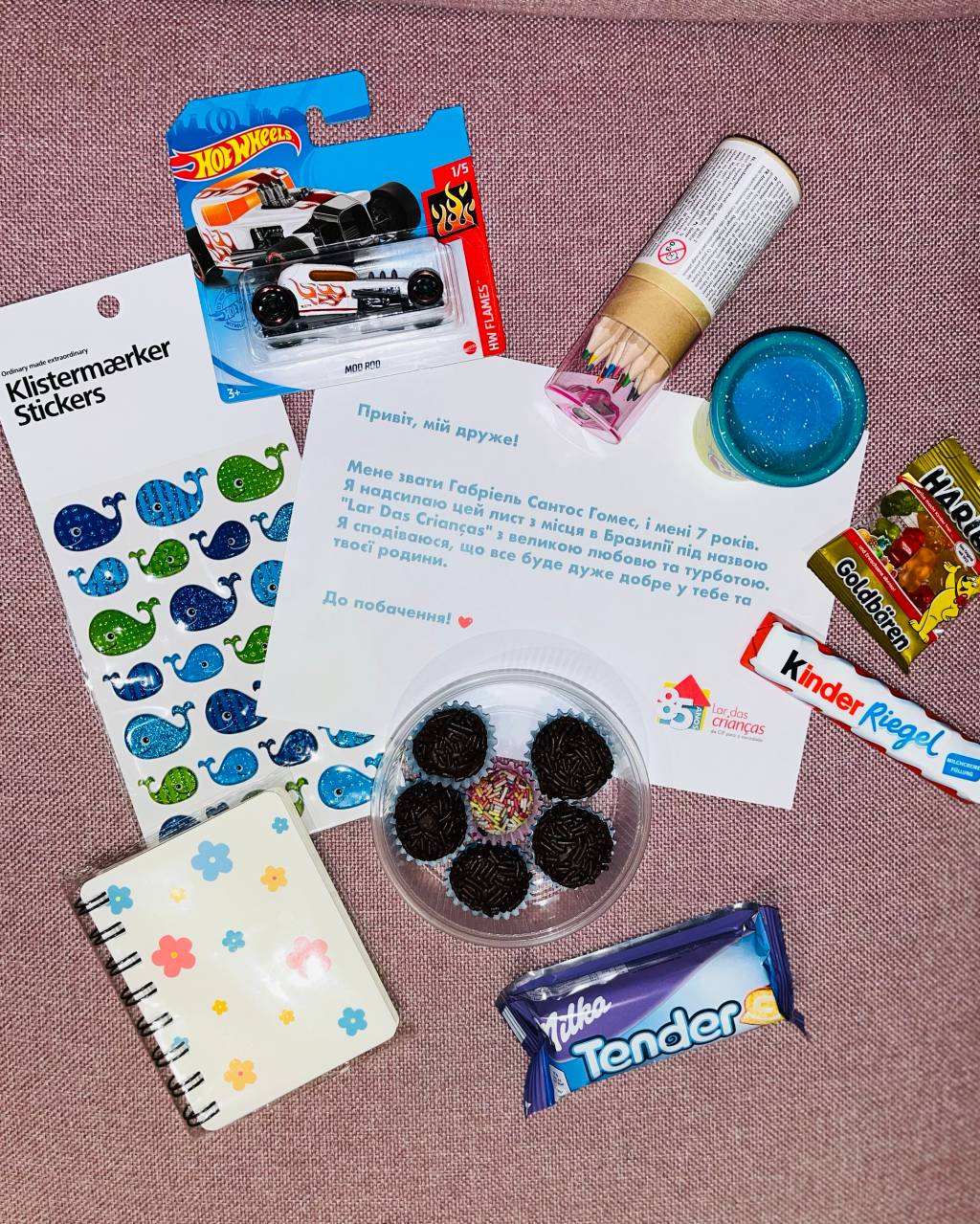 Abracinhos a Distância (Dinho Wolf, Meri Giorgobiani e Shelley Lui-Divulgação) Foto exibe itens inclusos em kit para crianças ucranianas, com brigadeiros, carrinho e carta.