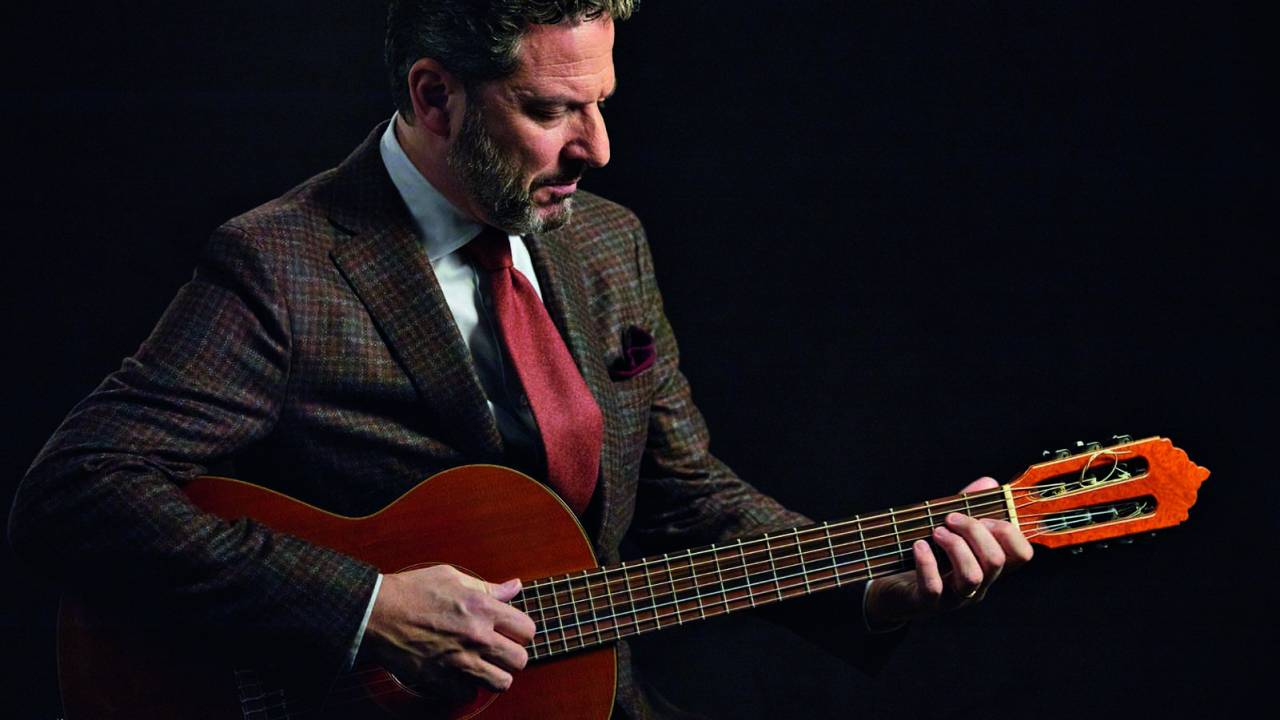 Imagem mostra homem de terno e gravata segurando um violão