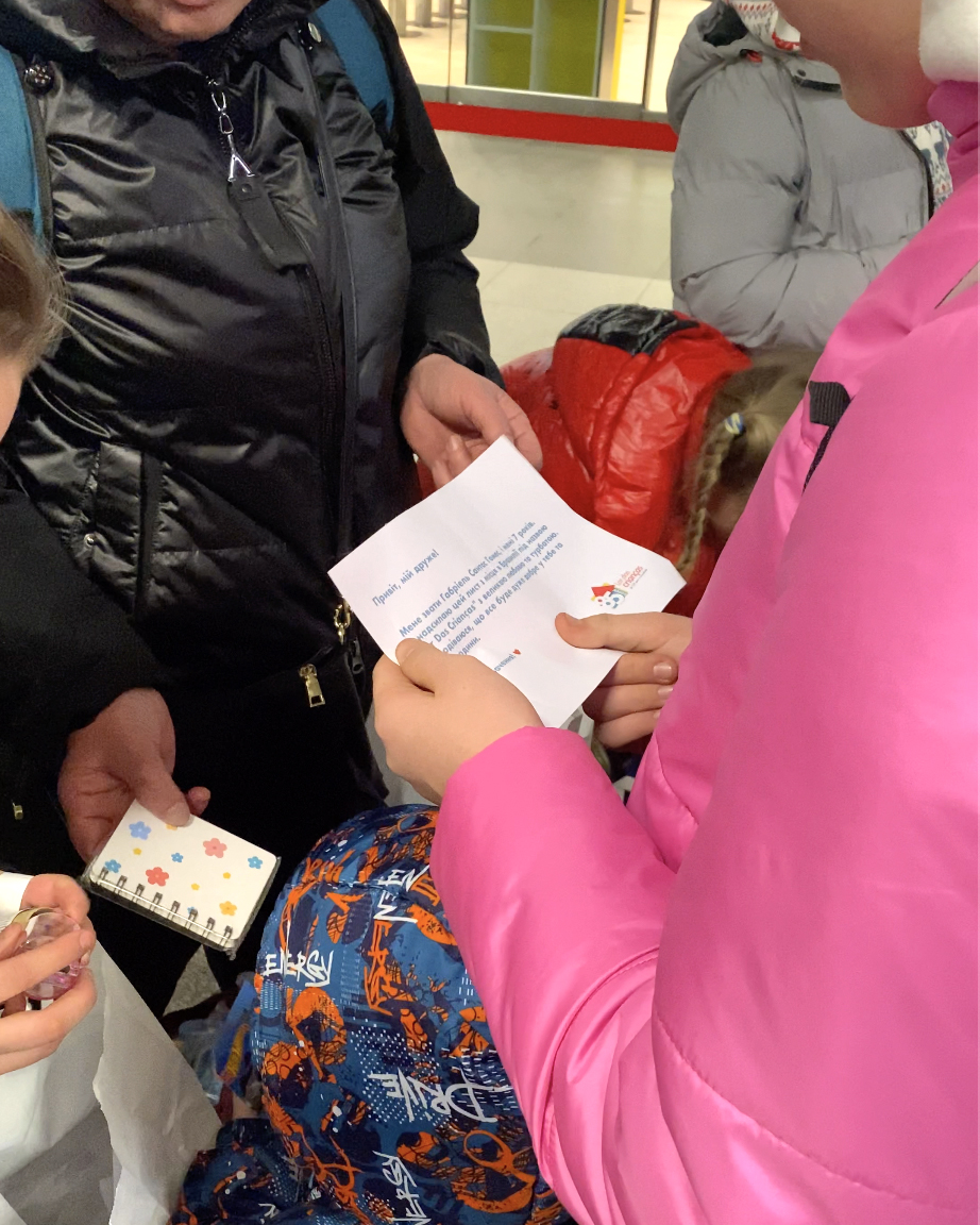 Abracinhos a Distância (Dinho Wolf, Meri Giorgobiani e Shelley Lui-Divulgação) Crianças ucranianas recebem kit com brindes e cartas em estação na Ucrânia. A foto exibe em detalhe uma mão segurando uma das cartas.