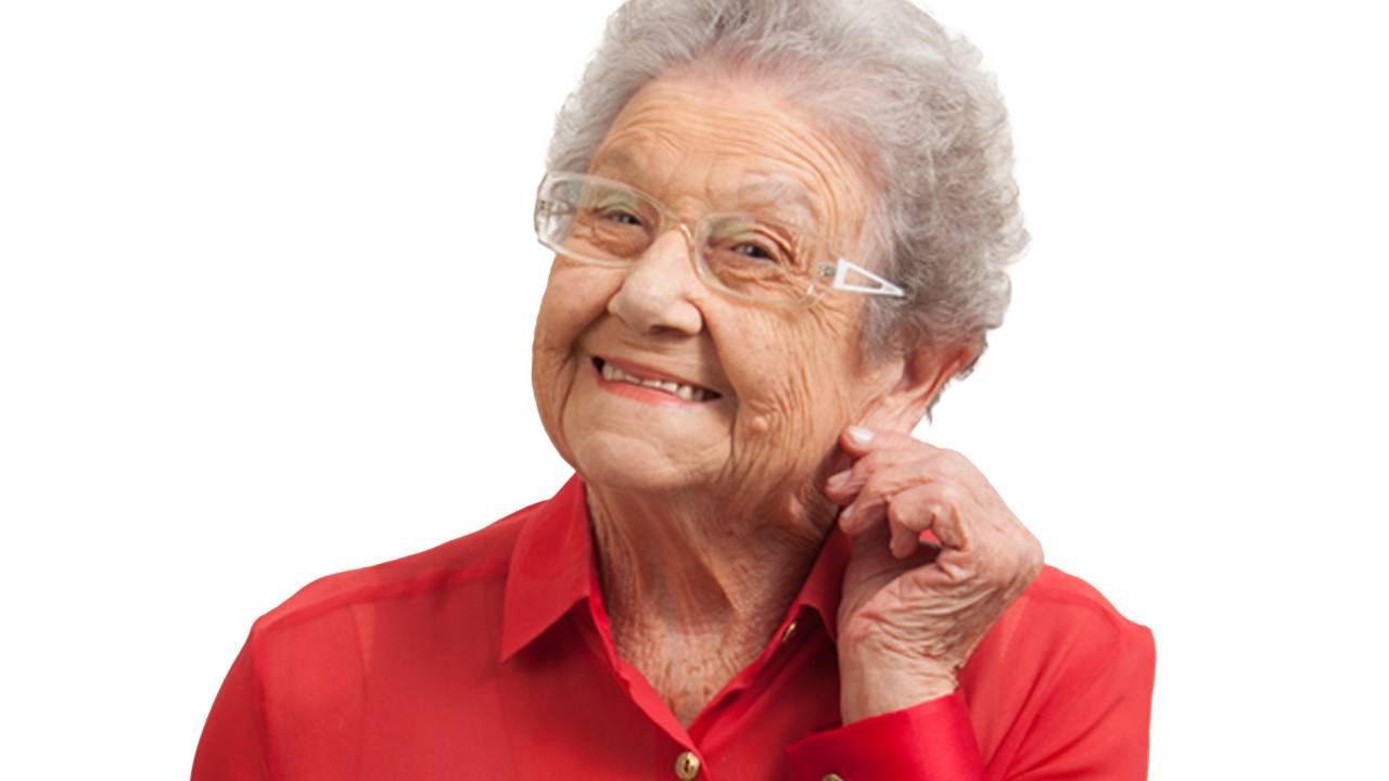 Palmirinha posa com uma mão puxando a orelha, sorrindo e vestindo camisa vermelha de botões dourados.