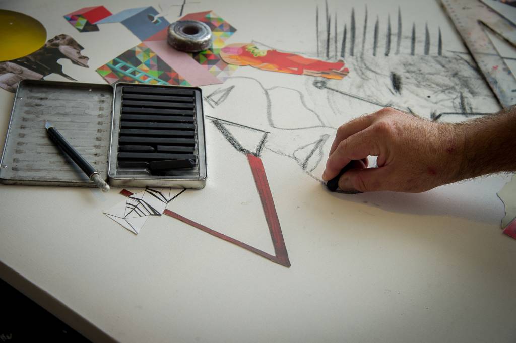 Vímerson Cavanilas (Rogério Pallatta) Imagem exibe detalhe de tela branca com alguns desenhos, lápis e a mão de Vímerson trabalhando na obra.