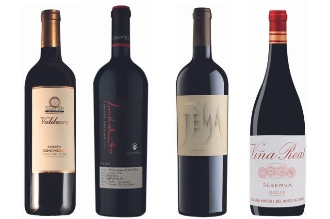 Quatro garrafas de diferentes vinhos tintos dispostas sobre fundo branco