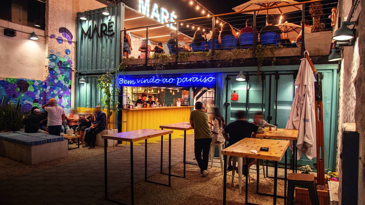 Ambiente de bar decorado por sinal de neon, containers e mesas altas