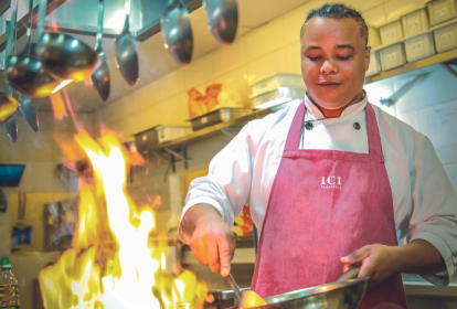 Imagem mostra homem cozinhando com frigideira na mão. Uma chama alta de um fogão é vista em primeiro plano