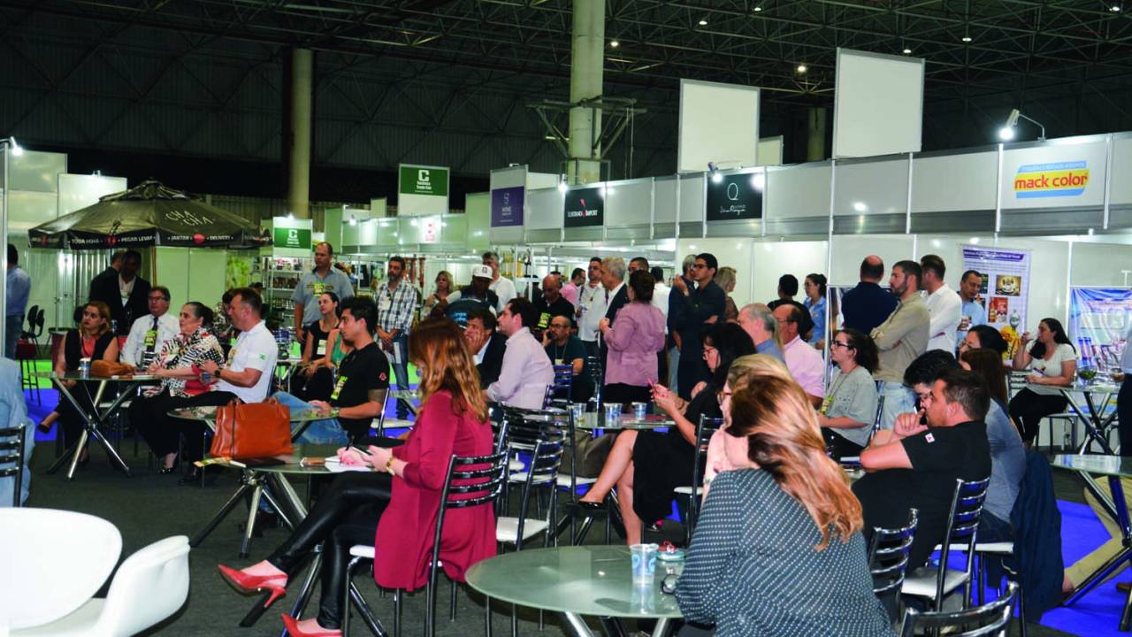 Evento com grande público sentado em cadeiras assistindo algo atentamente