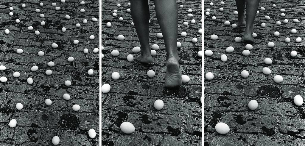 Entrevidas, da série Fotopoemação, 1981 Fotografia em impressão analógica 140 x 94 cm cada (tríptico) Coleção da artista Foto Henri Virgil Stahl.jpg Imagem em preto e branco mostra três fotos de chão com ovos. Na foto do meio, pernas de uma pessoa caminhando sobre o chão.
