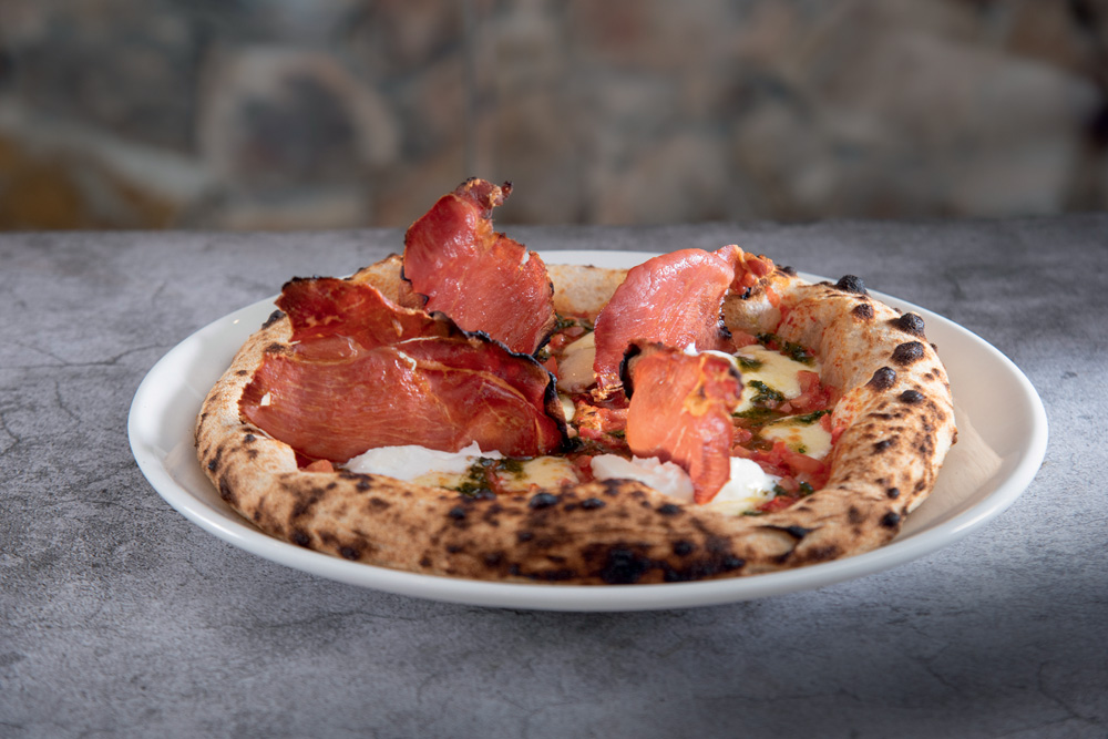 Pizza de massa grosa coberta por burrata, presunto cru e mais