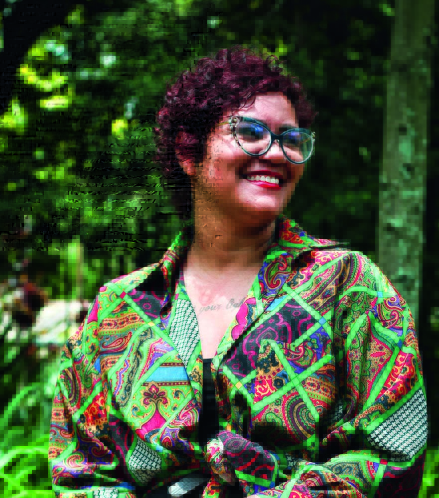 Jo Melo1.jpg Jo Melo posa sorrindo; ao fundo está um fundo verde repleto de natureza