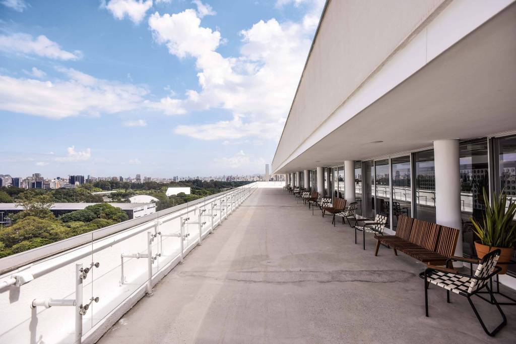 Vista aniversário Foto mostra sacada do MAC, onde fica o restaurante Vista. O céu está azul, com poucas nuvens. Cadeiras e mesas em tons terrosos estão no canto direito
