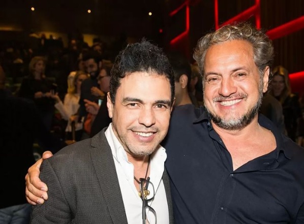 Imagem mostra Zezé di Camargo e Breno Silveira abraçados, sorrindo
