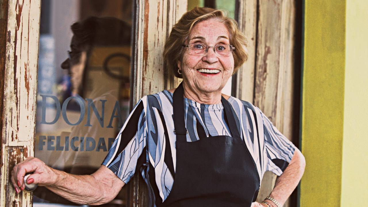 Mulher idosa posa em frente ao bar