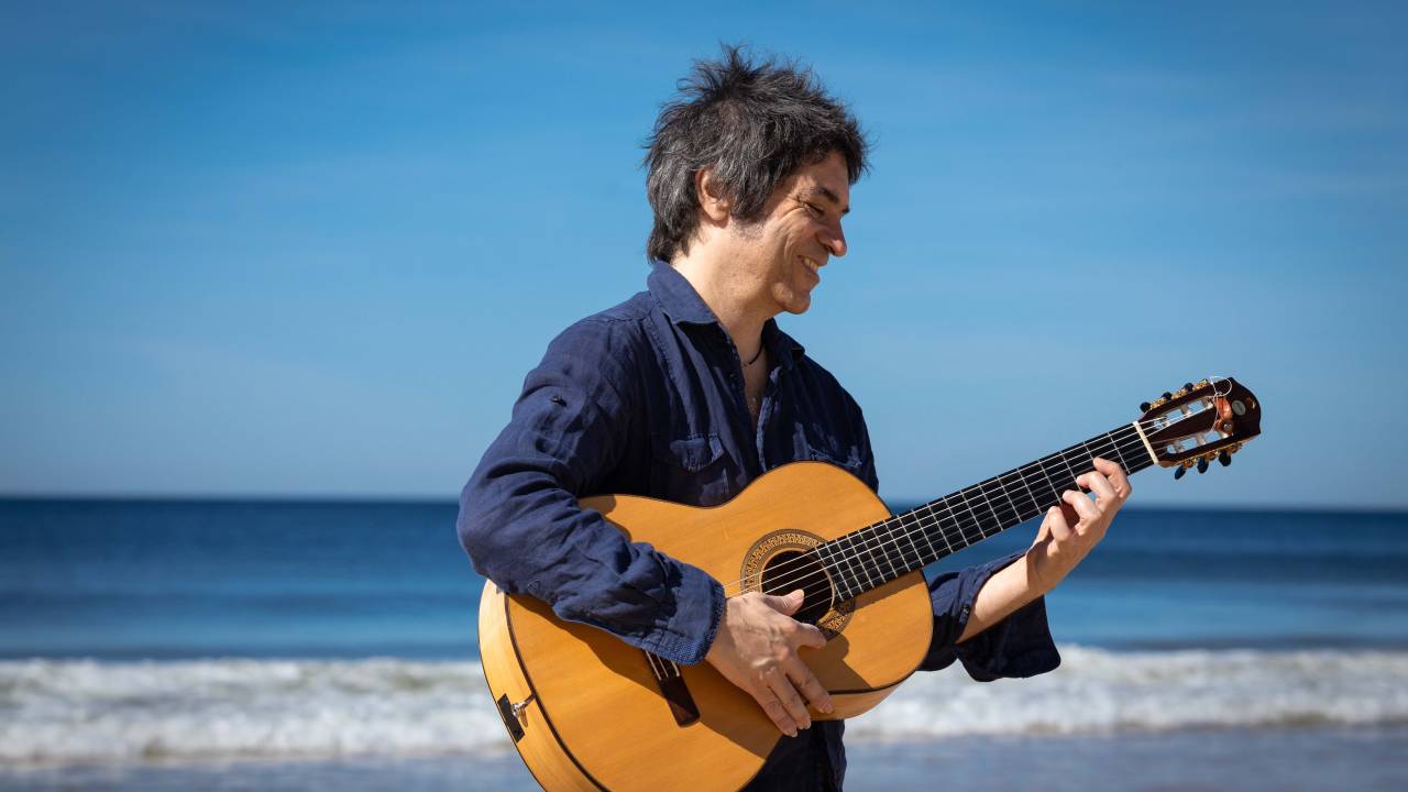 Imagem mostra homem na praia tocando violão, em pé