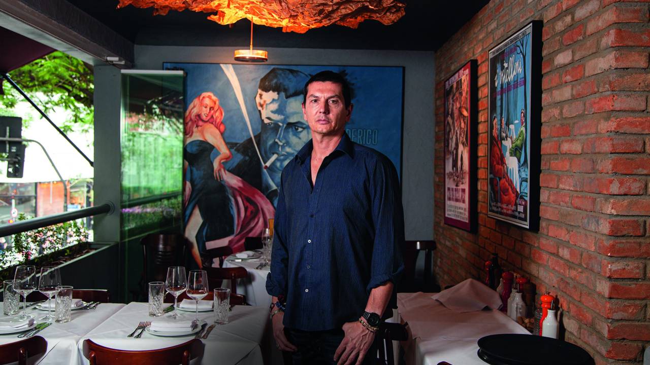 Imagem mostra homem de camisa em pé em salão de restaurante