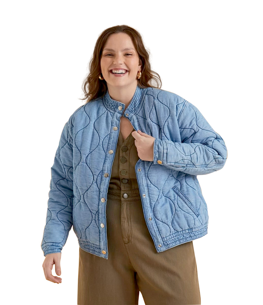 Modelo plus size branca, morena de cabelos lisos e compridos, usa jaqueta bomber jeans