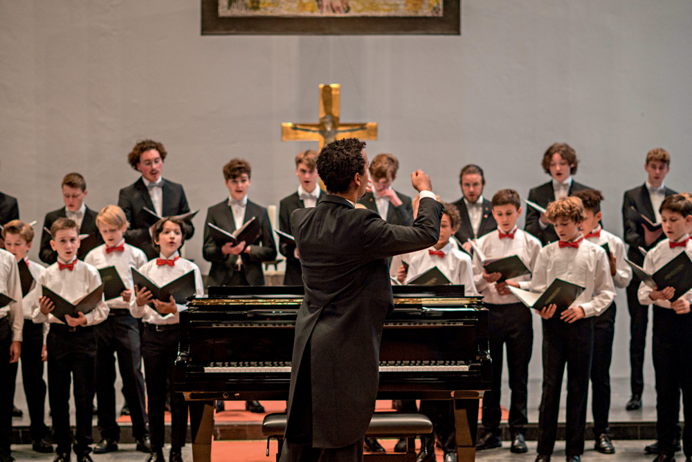 Meninos Cantores de Hamburgo.JPG Imagem mostra homem de terno de costas, regendo coro de crianças