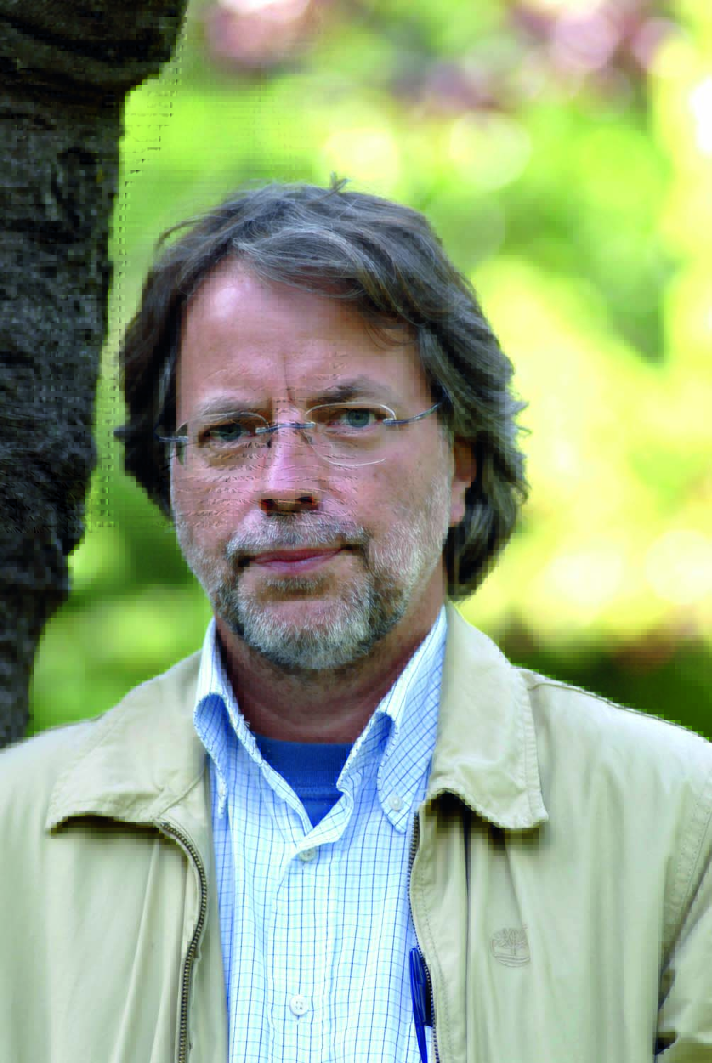 Mia Couto, escritor. Mia Couto é um homem de meia-idade, branco e magro, de cabelos e barba grisalhos. Tem olhos azuis, usa óculos e posa em um jardim do ombro para cima