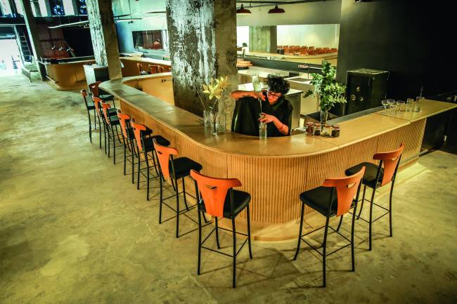 São Paulo 05 de julho 2022CORTINAFoto Alexandre Battibugli VSP Restaurante do Cortina, um balcão marrom com várias cadeiras altas. Uma funcionária trabalha no balcão