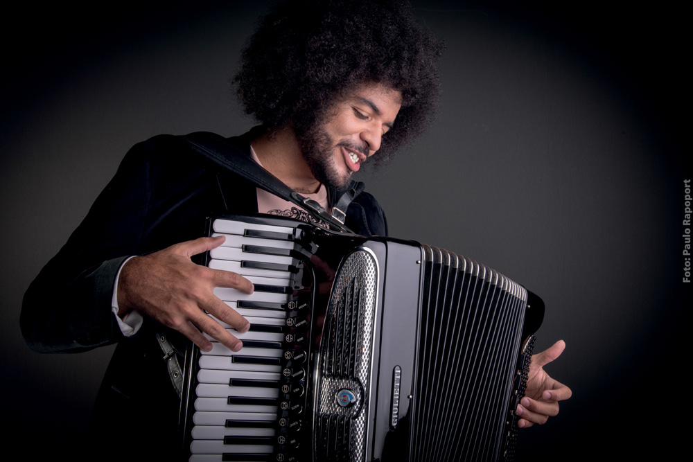 Imagem mostra homem sorrindo tocando sanfona