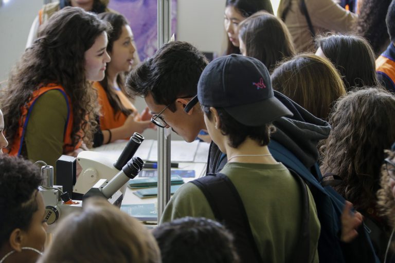 Jovens na 12ª Feira USP e as Profissões 2018, um deles com os olhos em um microscópio