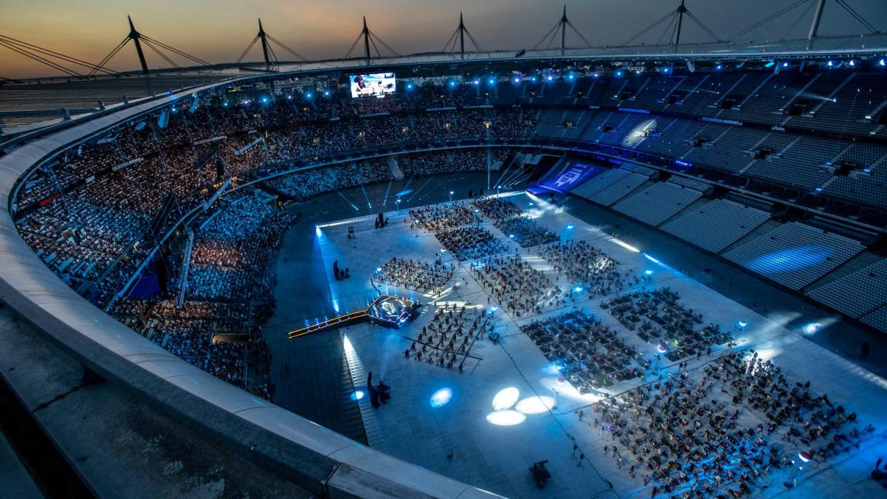 Imagem mostra estádio com multidão no centro e nas plateias