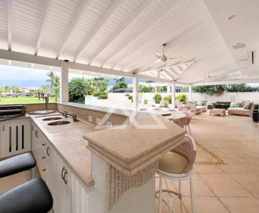 Casa tem área gourmet, cinco suítes e spa (Divulgação) Foto exibe área gourmet de mansão com balcão claro e cadeiras.