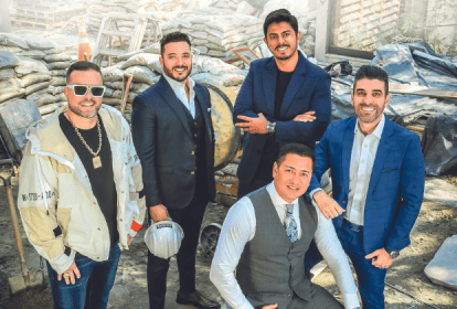 Imagem mostra cinco homens vestindo ternos e camisas em área de construção, sorrindo