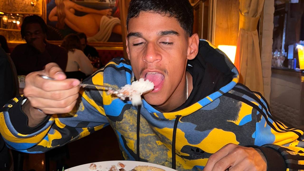 Luva de Pedreiro posa levando pedaço de comida à boca no restaurante Paris 6. À sua frente, prato com arroz, feijão e ovo frito