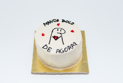 Bolo branco com a frase 'manda bolo de agora' e um personagem com corações ao redor.