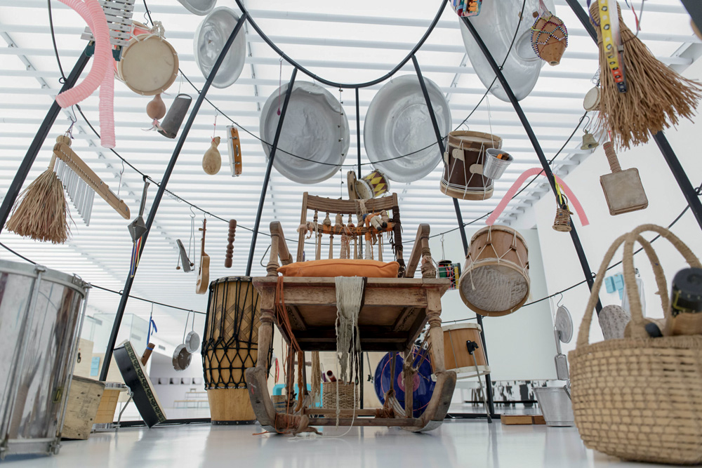 Crédito_ Mateus Lustosa_Divulgação.jpg Instalação de arte circular, com instrumentos diversos em volta. Há uma cadeira de balanço no meio