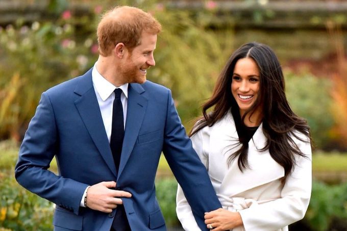 Harry e Meghan Markle posam andando e sorrindo, em frente a jardim