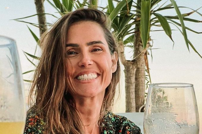 Foto da atriz Deborah Secco sorrindo, diante de fundo com árvores