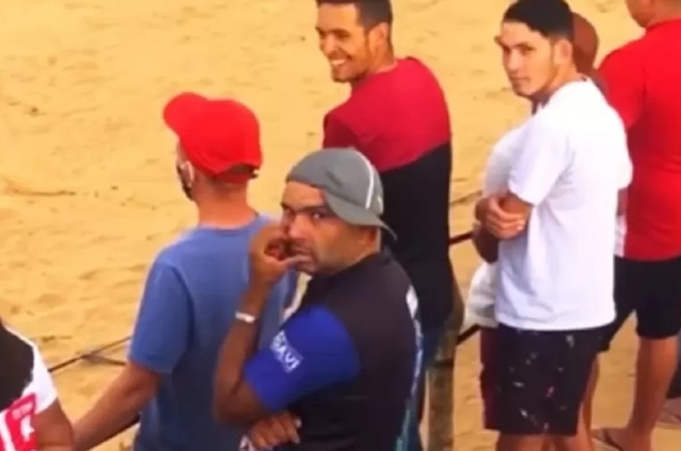 Quatro torcedores assistem partida em campo de terra. Torcedor do meio, Bill, olha para a câmera após ser chamado