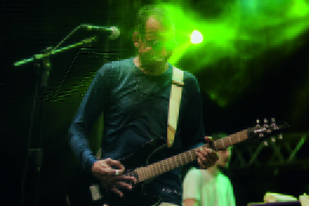 Imagem mostra homem sorrindo tocando guitarra com uma luz verde atrás de sua cabeça