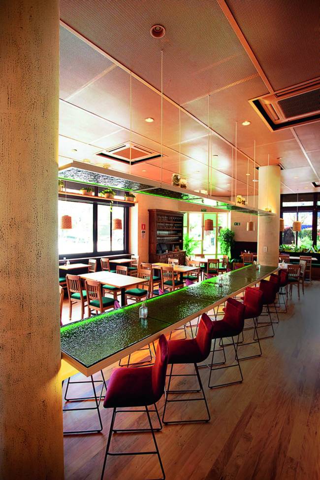 Ambiente Basilicata Pinheiros Ambiente interno de restaurante com mesas de tampo verde, amplas janelas e pilastras, sem nenhuma pessoa sentada às mesas