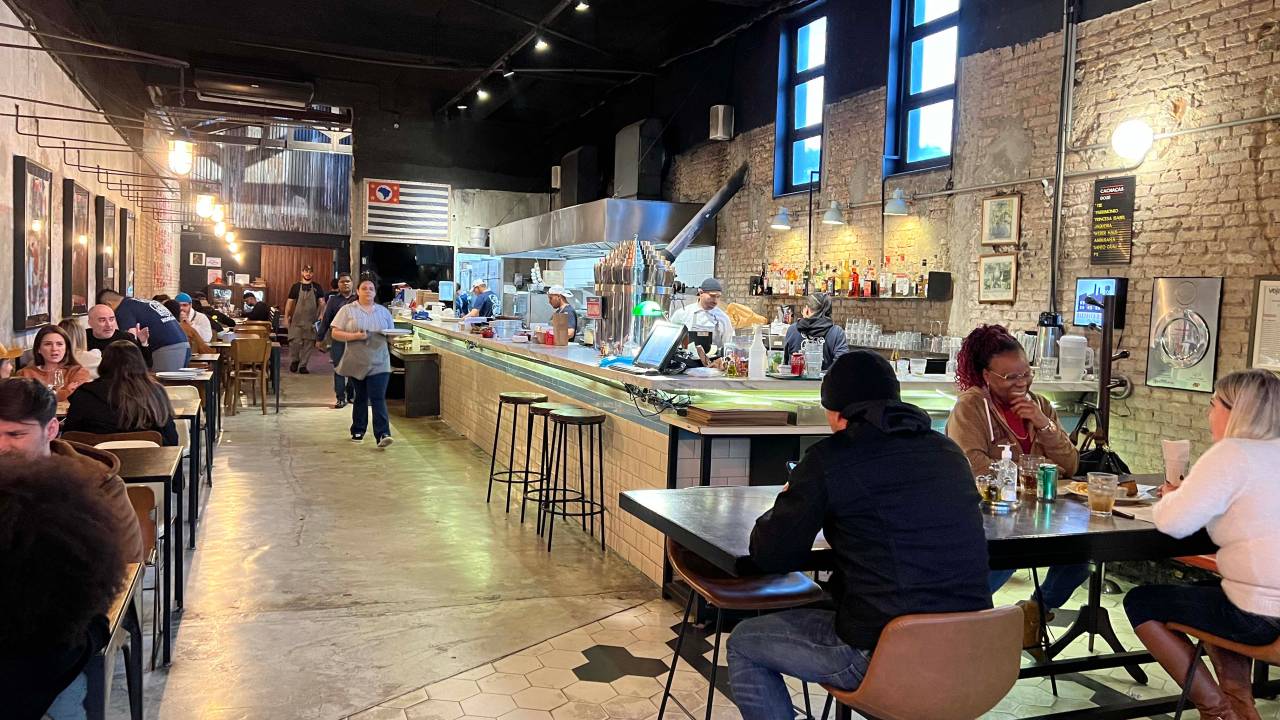 Ambiente interno de restaurante de piso claro e bem iluminado, com pessoas sentadas à mesa