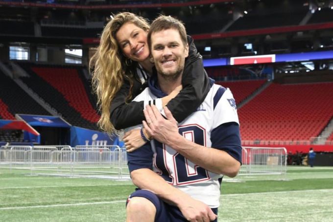 Gisele aparece abraçando Tom Brady que está agachado