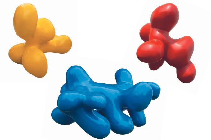 Três esculturas coloridas, uma azul, uma amarela e uma vermelha dispostas em um fundo branco. Elas têm formatos arredondados e adequados para subir em cima