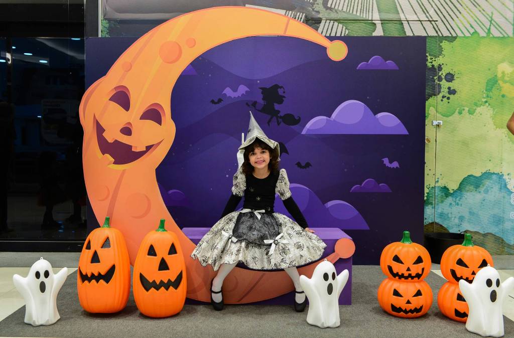 Shopping Vila Olímpia Halloween Espaço temático de Halloween com bonecos de abóbora e fantasmas. Menina fantasiada de bruxa está sentada no centro
