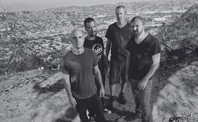 Imagem em preto e branco mostra quatro homens com uma cidade ao fundo