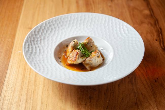 Dumpling de Peixe Mr. Wong Prato branco de porcelana sobre mesa de madeira contendo dumpling com recheio de peixe ao molho de missô