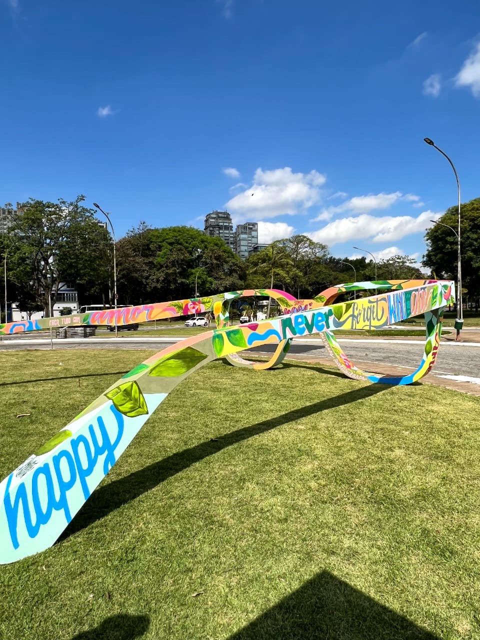 Obra de Agatha de Faveri para Chilli Beans (DIVULGAÇÃO) (1) Em gramado, foto exibe par de óculos coloridos gigantes com céu repleto de nuvens.